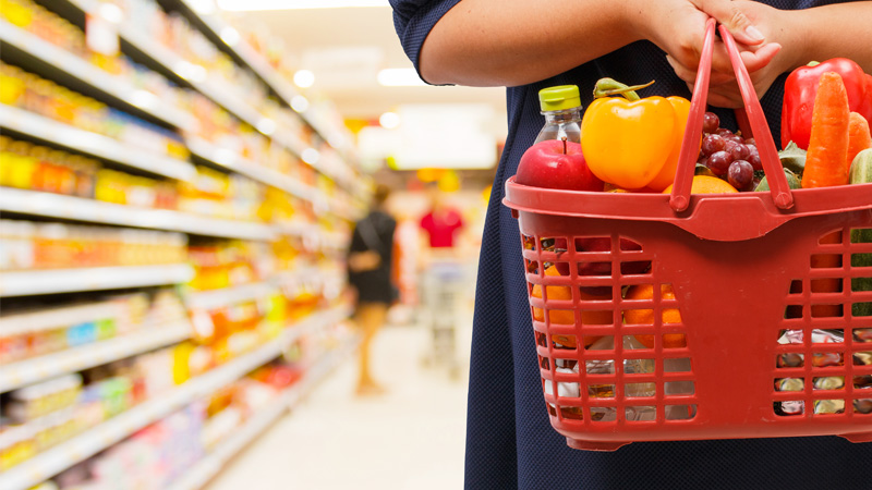 mani che portano un cestello della spesa con dentro i prodotti